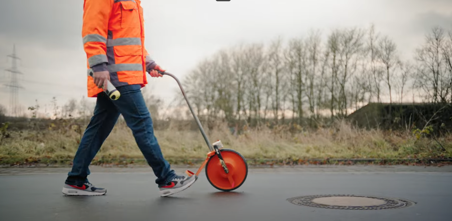 Ein Mann in einer orangen Warnjacke l&auml;uft &uuml;ber eine Strasse.