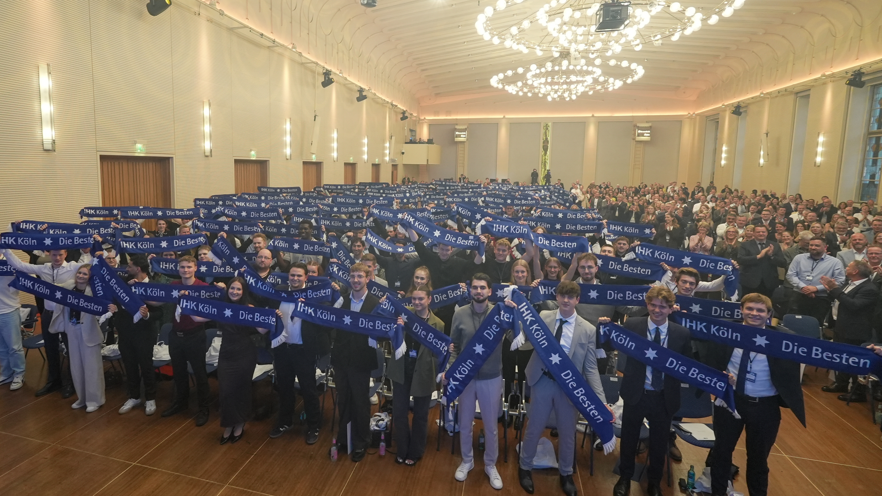 Eine Gruppe Auszubildender im Kölner Gürzenich hält Schals in die Luft. 