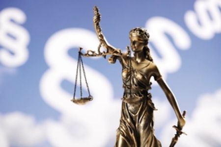 Justitia-Statuette vor Hintergrund mit Paragraphen