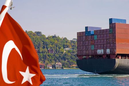 Man sieht die t&uuml;rkische Flagge und ein gro&szlig;es Containerschiff.