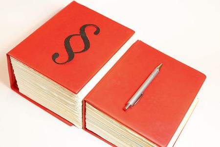 Zwei rote Gesetzb&uuml;cher liegen nebeneinander auf einem Tisch. Auf dem rechten von beiden befindet sich ein Kugelschreiber.