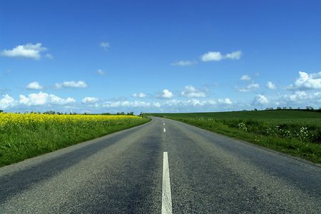 Landstra&szlig;e f&uuml;hrt an Feldern vorbei, zwei Windr&auml;der im Hintergrund