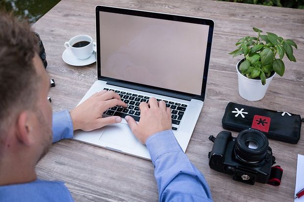 Mann am Arbeitsplatz am PC mit Kamera und Kaffeetasse