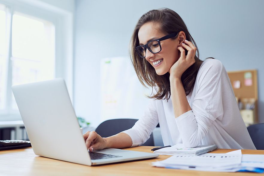 Frau sitzt an einem Schreibtisch und arbeitet am Laptop
