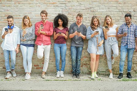 junge Menschen verschiedener Herkunft lehnen an einer Hauswand und blicken auf ihre Smartphones