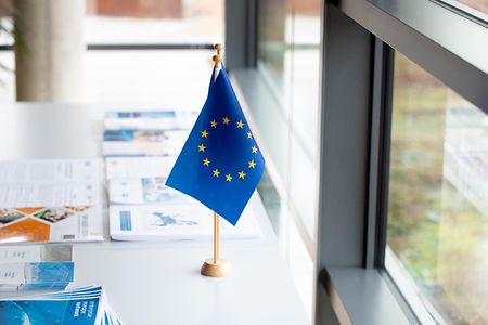 Europaflagge steht auf einem Tisch umgeben von Unterlagen und Brosch&uuml;ren 