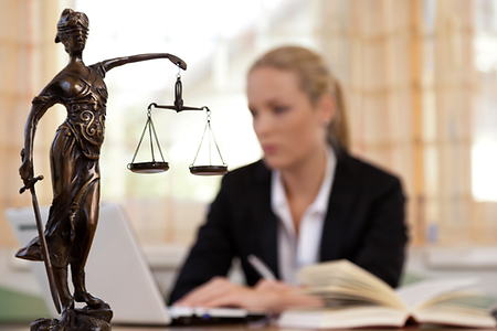Anwältin sitzt am Laptop, im Vordergrund die Justitia