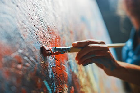 Hand, die mit Pinsel Farbe auf Leinwand aufträgt