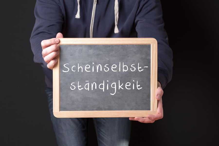 Arbeiter hält eine Tafel hoch auf der Scheinselbständigkeit steht
