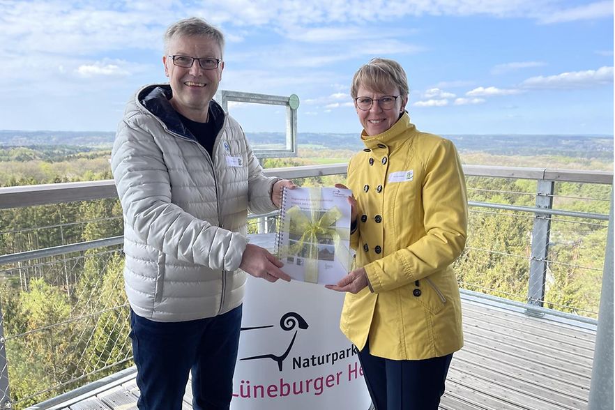 Olaf Muus (l.) und Monika Scherf stehen auf einer Aussichtsplattform und halten eine Urkunde.