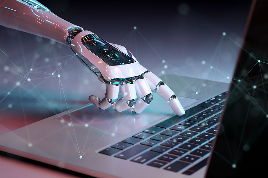 Hand eines Roboters schreibt am Laptop