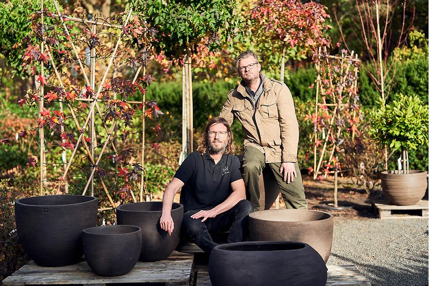 Thomas und Jens Sandau auf einer Terrasse mit gr&uuml;nen B&uuml;schen.