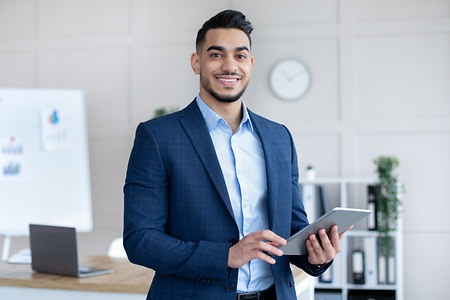 Happy male office worker in formal suit holding tablet computer and smiling at camera in modern office