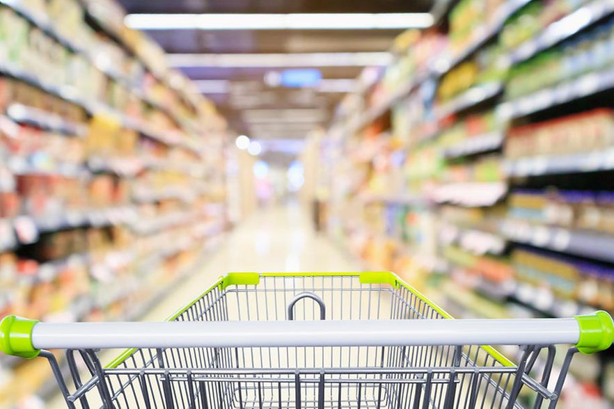 Einkaufswagen vor Hintergrunddarstellung eines Supermarktganges