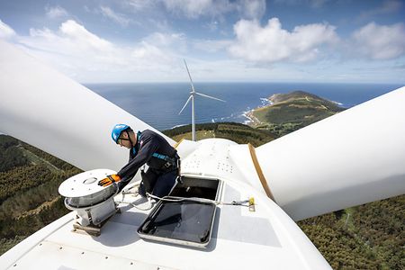Techniker arbeitet auf Windkraftanlage mit Blick auf Meer und Landschaft.