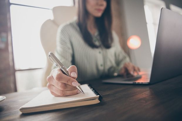 Frau schreibt mit Kulli auf Arbeitsblock am Tisch