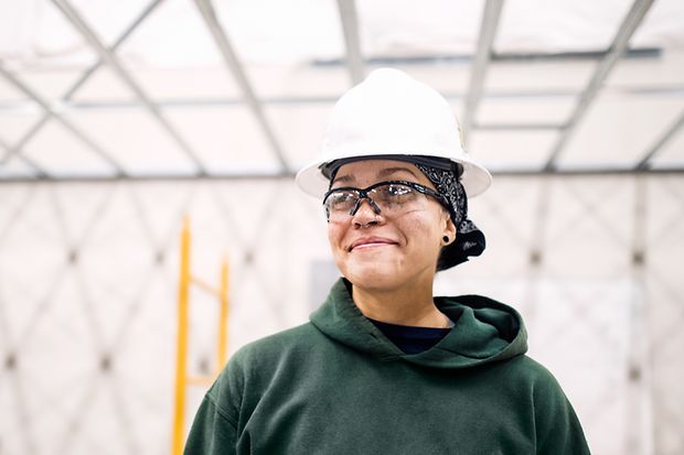 Eine Frau mit Schutzbrille und Helm steht auf einer Baustelle