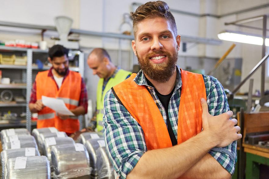 Gl&uuml;cklicher Lagerarbeiter in der Ausbildung im Material Lager der Metallfabrik mit Kollegen