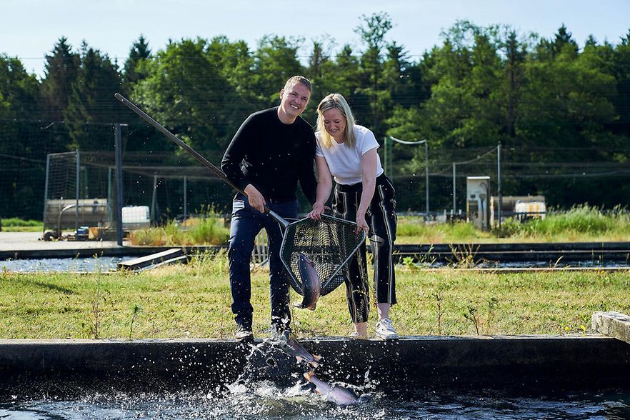 Stephan und Heide Winkelmann stehen mit einem Kescher am Beckenrand und holen eine Forelle aus dem Wasser.