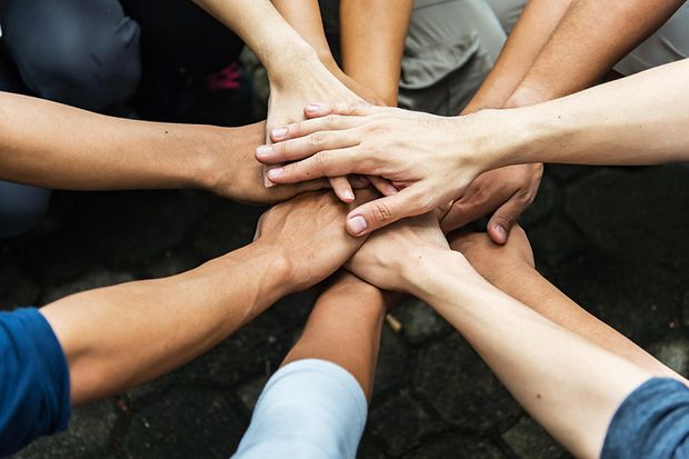 Menschen hocken im Kreis und legen ihre H&auml;nde &uuml;bereinander