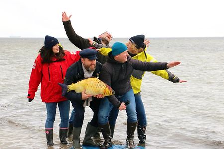 Das Team von Fangfrische Baufinanzierung am Strand mit einem Fisch