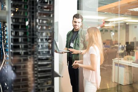 Two,Business,People,Standing,In,Server,Room,With,Laptop,And