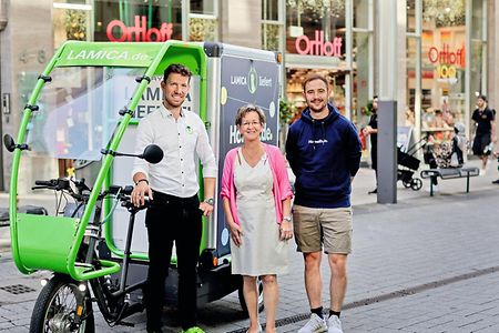 Stefan Schneider, Sabine Gerberich und Michael M&uuml;ller stehen mit einem Lastenrad vor der Ortloff-Filliale am K&ouml;lner Neumarkt