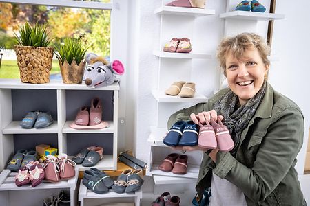 Iris Mesebrink vor einem Regal mit Kinderschuhen, sie h&auml;lt zwei Paare in ihrer rechten Hand.