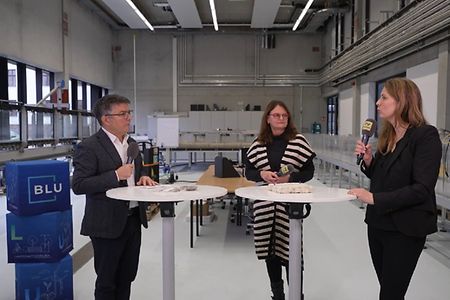 1 Mann und 2 Frauen im Interview an einem Tisch stehend mit Mikrofon in der Hand