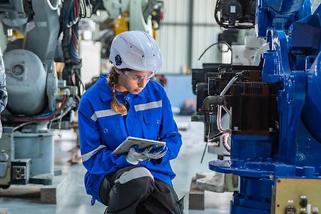 Eine Frau im Blaumann kontrolliert eine Industrieanlage