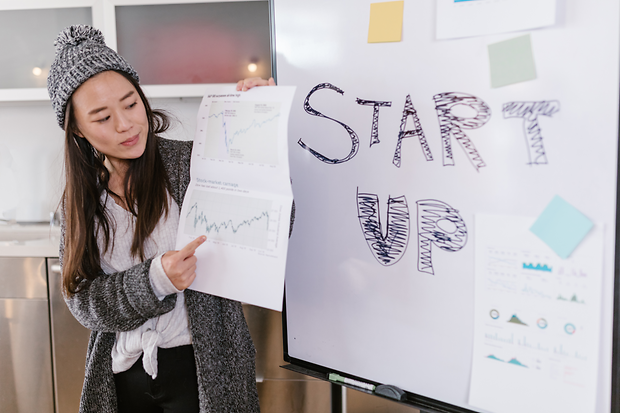 Eine junge Frau hält ein Diagramm in der Hand. Sie steht vor einem Flipboard, auf dem Start-up steht