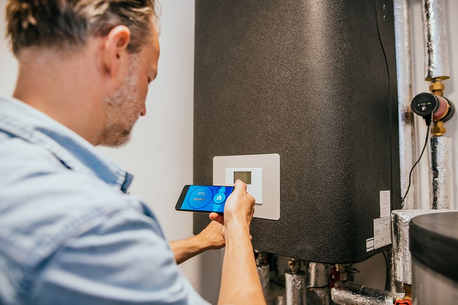 Mann kontrolliert die Heizwärme mit Hilfe einer App auf dem Smartphone