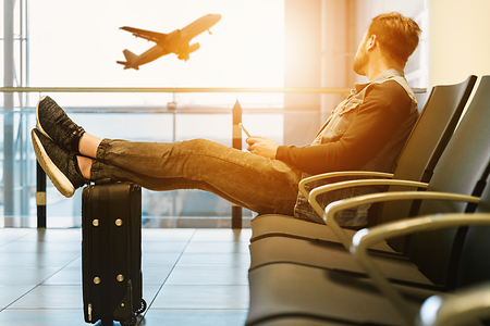 Junger Mann sitzt am Flughafen und beobachtet Flugzeuge