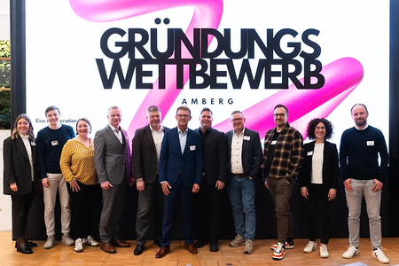 Eine Gruppe von Männern und einigen Frauen vor einem Banner des Gründungswettbewerbs Amberg