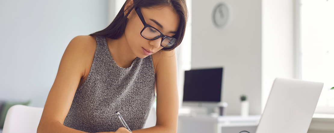 Ausbildungsnachweis Junge Frau, die an ihrem Tisch am Laptop sitzt, neben dem Bücher und ein Kaffee stehen
