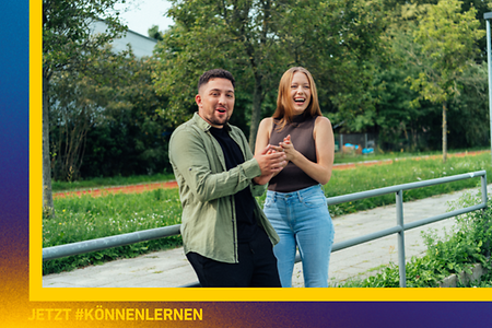 Zwei junge Azubis stehen draußen auf einer Wiese und freuen sich. 