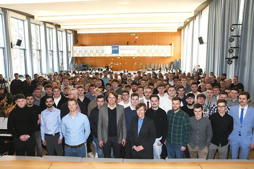 Absolvierende der Ausbildungswinterpr&uuml;fungen aus Bielefeld und G&uuml;tersloh stehen vor der B&uuml;hne in der Aula.