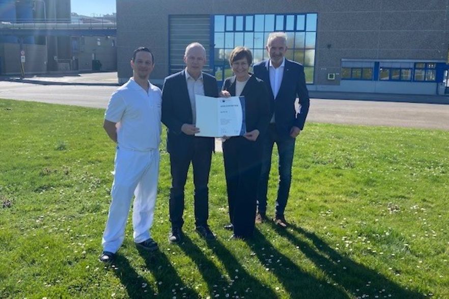 Vier Akteure stehen auf einer Wiese vor dem Firmengeb&auml;ude mit der Urkunde "IHK-anerkannter" Ausbildungsbetrieb in der Hand