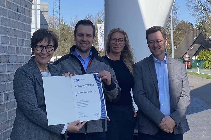 Die Beteiligten stehen vor der Firma W&ouml;rmann Team GmbH und halten die Urkunde "IHK-anerkannter Ausbildungsbetrieb" in die Kamera