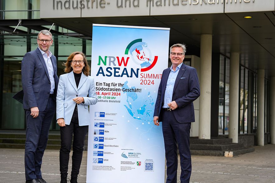 Drei Personen stehen vor der IHK neben einem Roll-up f&uuml;r den NRW-ASEAN Summit 2024 &ndash; Fokus auf internationale Wirtschaft.