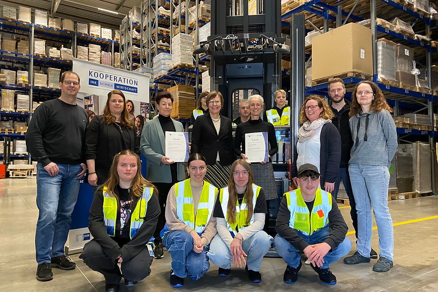 Gruppenfoto in einem Logistiklager mit Gabelstapler &ndash; &Uuml;bergabe von IHK-Urkunden im Rahmen einer Schulkooperation