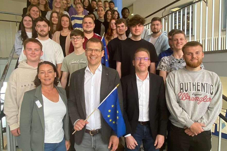 Gro&szlig;e Gruppe Jugendlicher mit mehreren Erwachsenen auf einer Treppe &ndash; vorne wird eine Europaflagge pr&auml;sentiert.