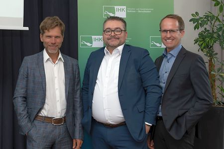Drei M&auml;nner stehen vor einem IHK Roll-up und l&auml;cheln in die Kamera.