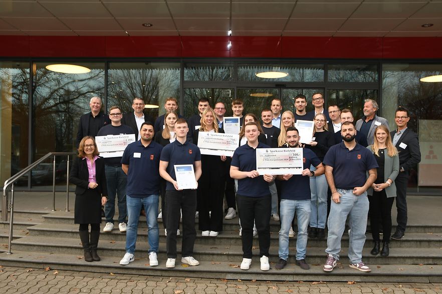 Gruppenfoto mit IHK-Vertretern und den teilnehmenden Auszubildenden. Einige halten Schecks in der Hand.