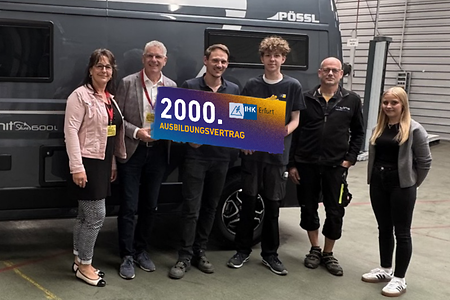 Mehrere Personen stehen nebeneinander, lächeln und halten ein Schild in den Händen. Aufschrift: 2000. Ausbildungsvertrag.