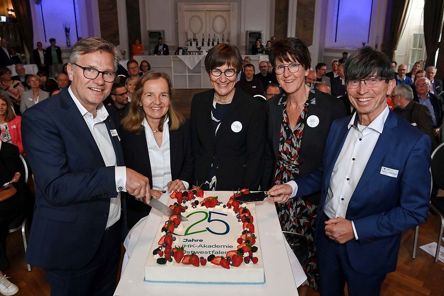 F&uuml;nf Personen schneiden gemeinsam eine gro&szlig;e Torte zum 25-j&auml;hrigen Jubil&auml;um der IHK Akademie Ostwestfalen an.