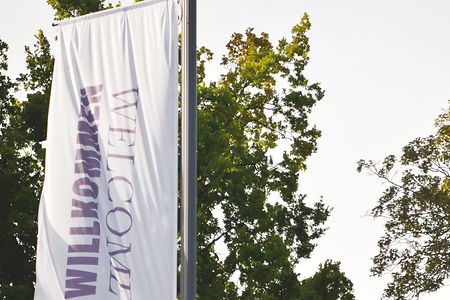 Fahne mit der Aufschrift Willkommen flattert an einem Fahnenmast