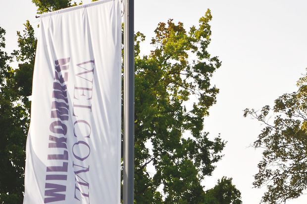 Fahne mit der Aufschrift Willkommen flattert an einem Fahnenmast