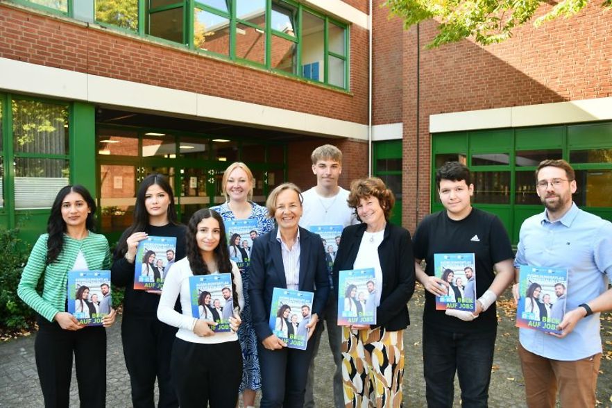 Sch&uuml;ler und Erwachsene pr&auml;sentieren Ausbildungsatlas vor Schule.