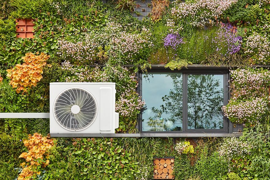 W&auml;rmepumpe h&auml;ngt an einem Haus, dessen Fassade bepflanzt ist